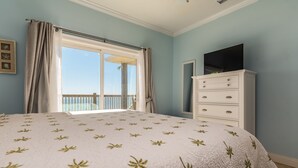 A bedroom with a large bed, a dresser, a TV, and a balcony with a view.