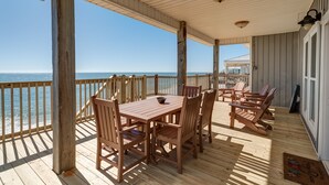A wooden deck with a table and chairs, overlooking the ocean.