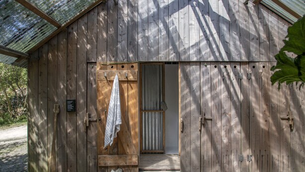 Un edificio de madera rústica con una puerta grande, un escalón pequeño que lleva a la entrada y una toalla colgada en la puerta.