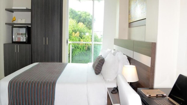 A hotel room with a bed, a nightstand, a desk, a wardrobe, and a balcony with a view of greenery. - hotel metropolitano plaza (Valledupar)
