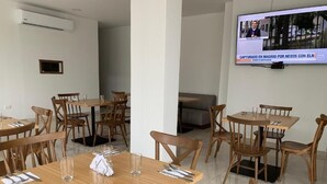 A dining area with wooden tables and chairs, a TV screen displaying a news program, and a tiled floor. - hotel metropolitano plaza (Valledupar)