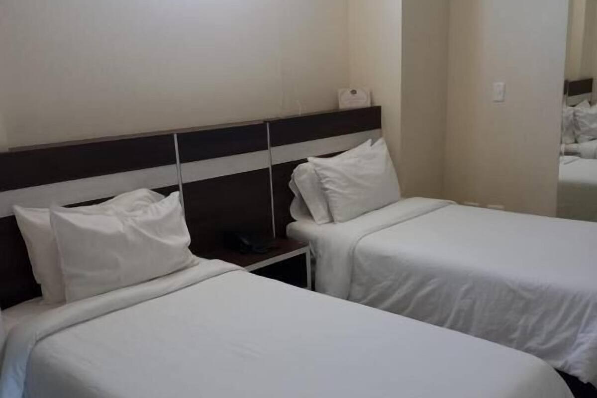 Hotellihuone, jossa on kaksi erillistä sänkyä, yöpöytä, ikkuna ja peili.