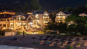 A coastal hotel with multiple buildings, a beach with umbrellas, and a mountain in the background. - The Black Pearl Villas (Sithonia)