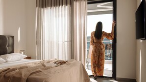A hotel room with a bed, a flat-screen TV, and a balcony with a view. - The Black Pearl Villas (Sithonia)