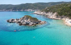 A coastal landscape with a rocky island surrounded by clear turquoise waters and a sandy beach.