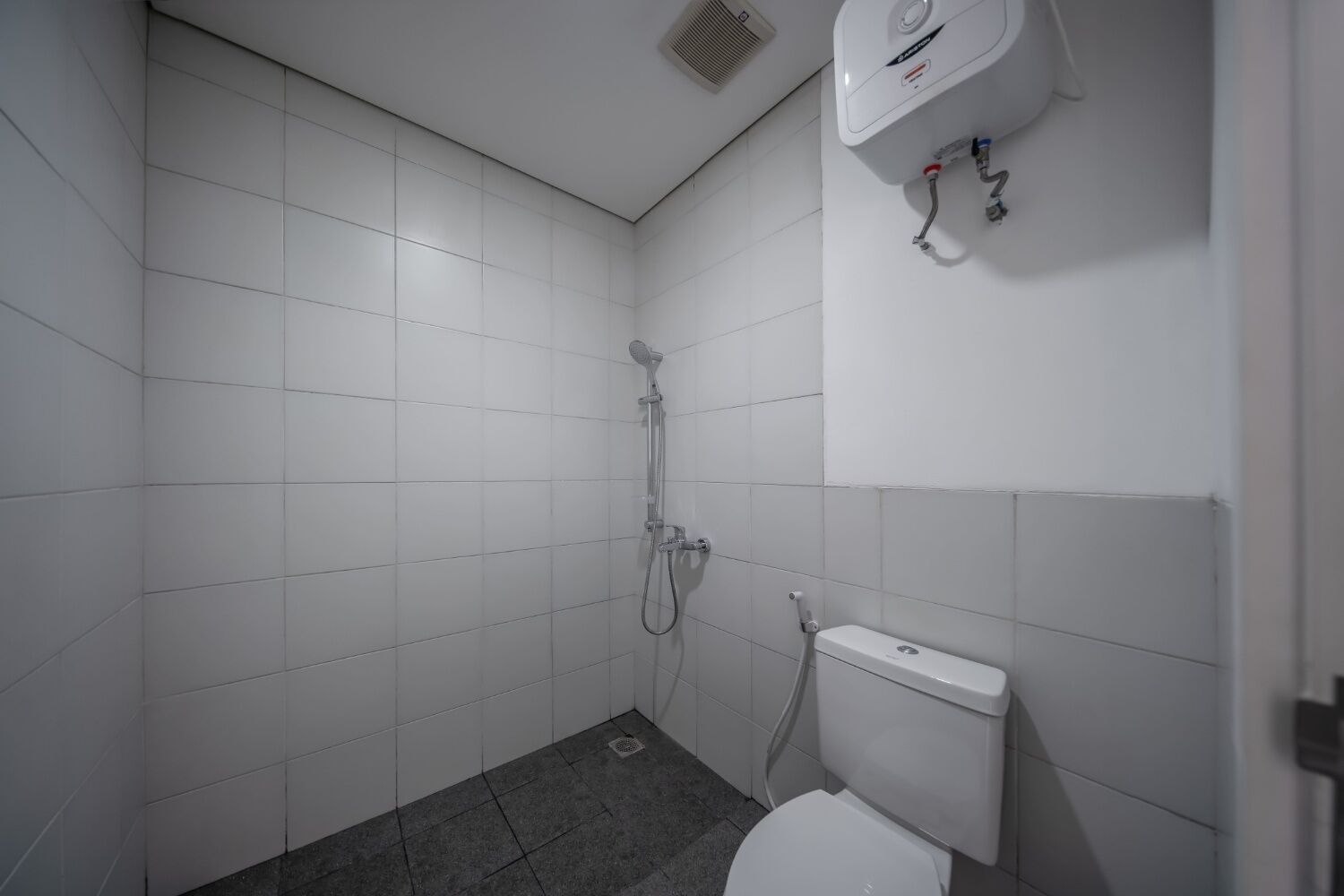Un baño pequeño y moderno con azulejos blancos, ducha e inodoro.