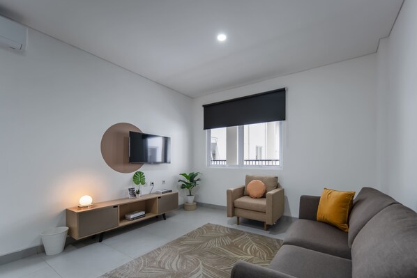 A modern living room with a flat-screen TV, a sofa, a chair, a coffee table, a side table, and a potted plant.