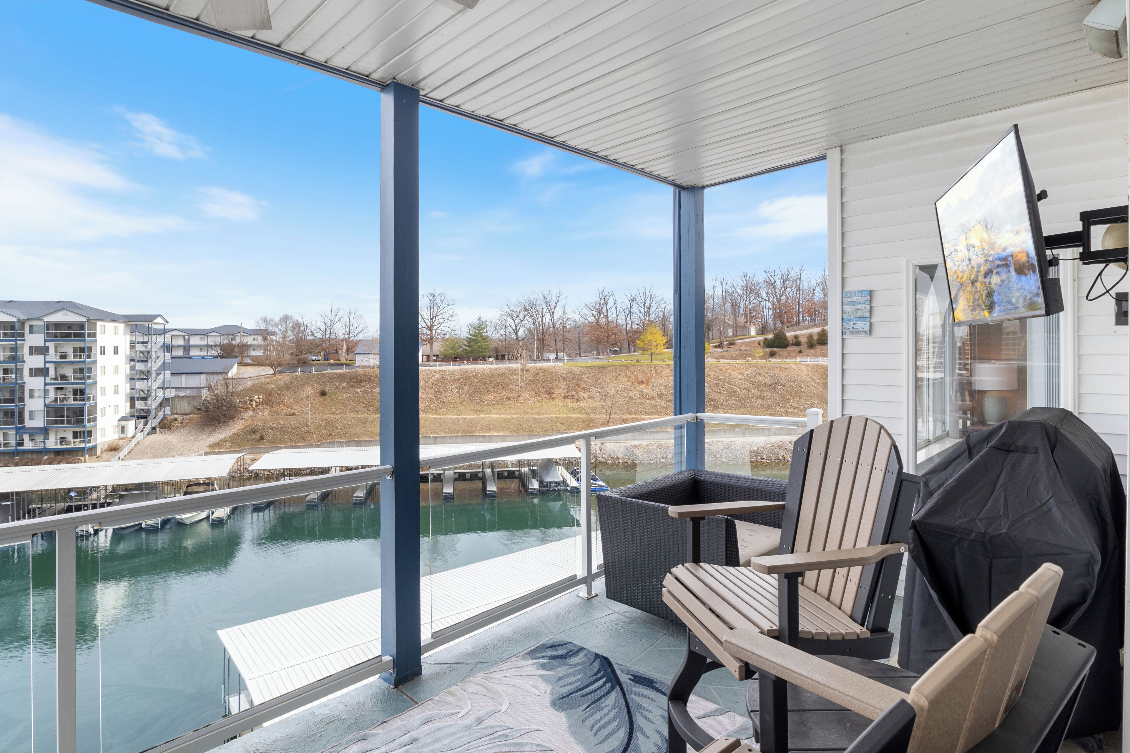 A covered outdoor area with a view of a river, a grill, and a seating area with chairs.