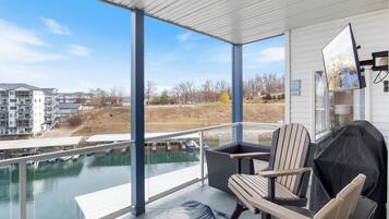 A covered outdoor area with a view of a river, a grill, and a seating area with chairs.