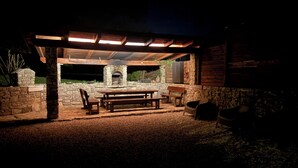 An outdoor patio with stone walls, a wooden table, benches, and a stone fireplace.