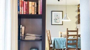 Une pièce avec une bibliothèque remplie de livres, une table à manger avec des chaises et un escalier menant à un autre niveau.