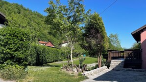 Une cour pavée de pierres, avec une clôture en bois, un arbre et un bâtiment doté d’un toit rouge.