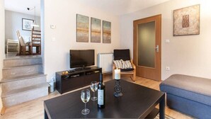 Un salon moderne avec un téléviseur à écran plat, une table basse avec des verres à vin, un canapé et des œuvres d’art accrochées au mur.