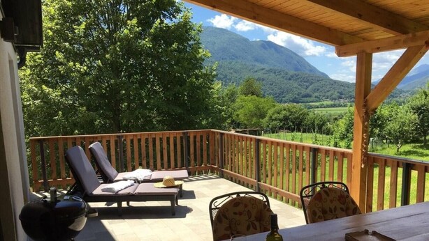 A covered outdoor seating area with lounge chairs, a table with wine glasses, and a grill. - Modern and renovated house in the beautiful Soca Valley (Kobarid)