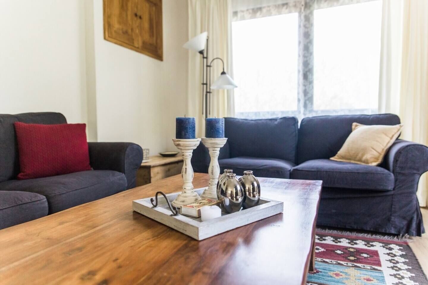 Een woonkamer met een houten salontafel, twee donkere banken, een rode kussen en een kamerbreed tapijt.