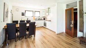 A modern kitchen with white cabinets, a dining area with a wooden table and chairs, and a wooden floor. - Modern and renovated house in the beautiful Soca Valley (Kobarid)
