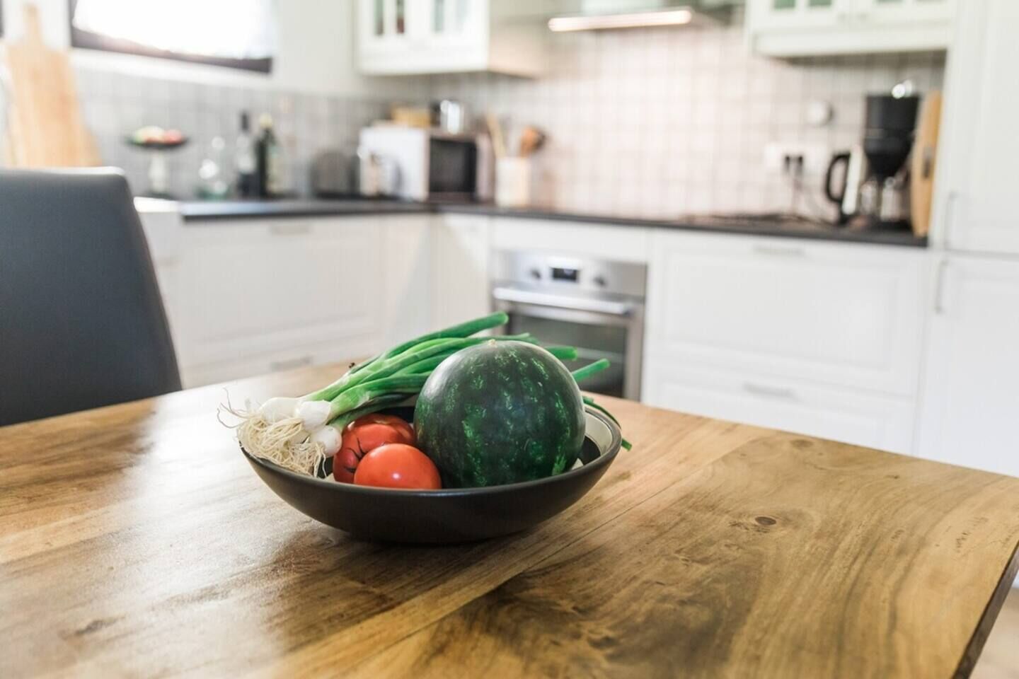 Une cuisine avec une table en bois sur laquelle se trouve un saladier rempli de légumes frais.