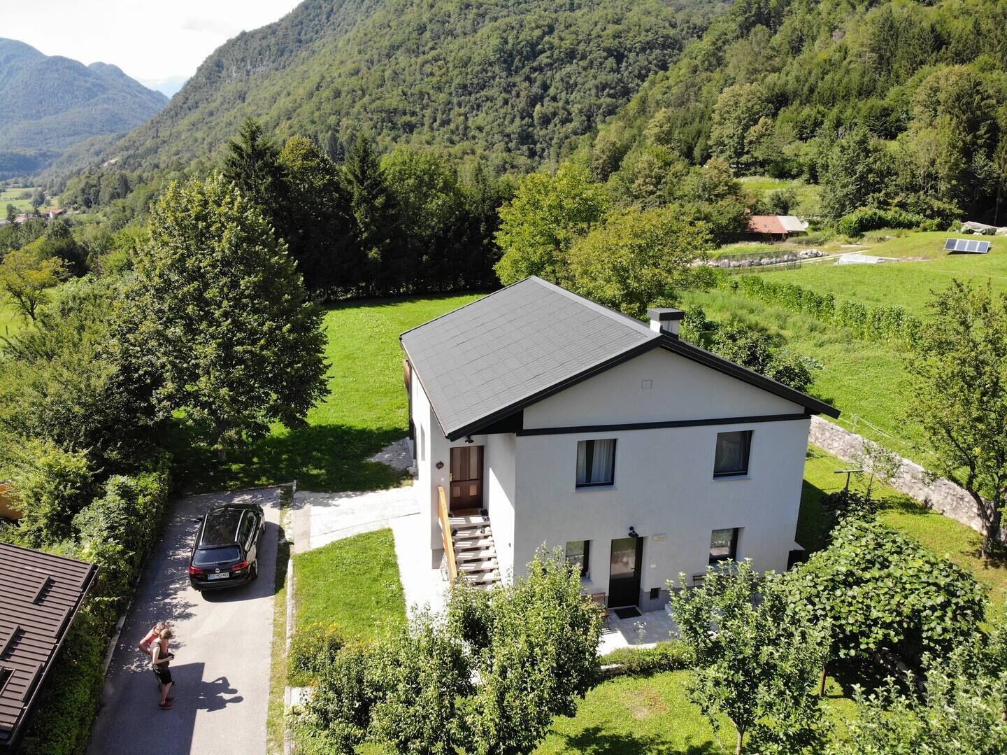 Un edificio bianco a due piani con tetto spiovente, immerso in campi verdi e alberi.