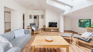 A spacious living room with a high ceiling, a wooden coffee table, grey sofas, and a TV on a wooden stand. - Stylish apartment 100 m2 in Vila with lake view , sleeps 6, 2 bedrooms, airco, balcony (Most na Soči)