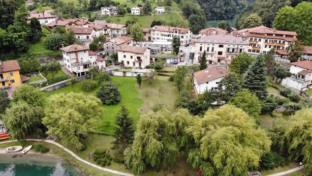 An aerial view of a lakeside residential area with houses, greenery, and a clear view of the lake.