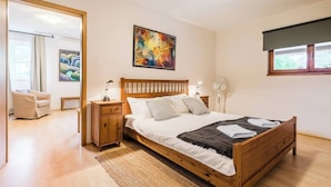 A bedroom with a wooden bed, a bedside table, a chair, a floor lamp, and a painting on the wall.