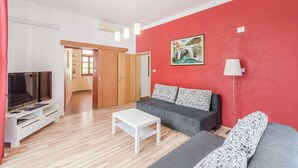 A living room with a red wall, a grey sofa, a white coffee table, and a TV on a white stand. - Apartma Most - accommodation with breathtaking views of the rivers, village and mountains (Most na Soči)