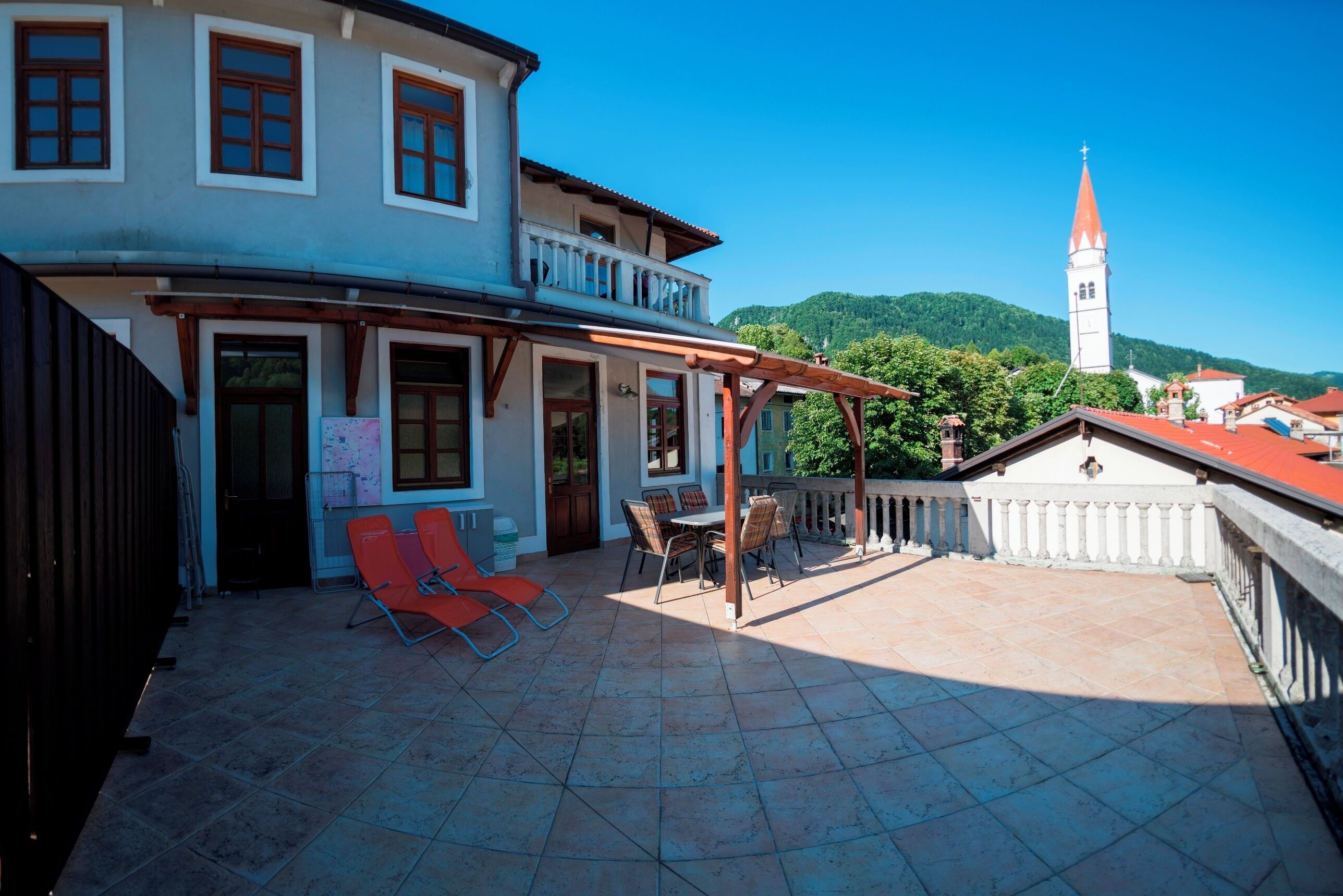 A two-story building with a balcony, outdoor seating area, and a view of a church tower.