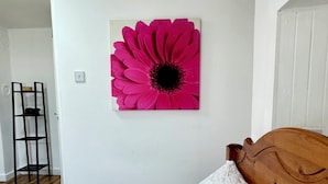 Un dormitorio con una cama, cabecera de madera, pared blanca y un cuadro grande de una flor rosa.