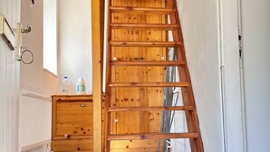 Una escalera de madera que sube a un piso superior, con un radiador y una pequeña mesa con objetos encima.