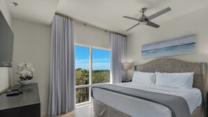 Une chambre d’hôtel avec un lit, un bureau, un ventilateur de plafond, une vue sur l’extérieur et un tableau au mur.