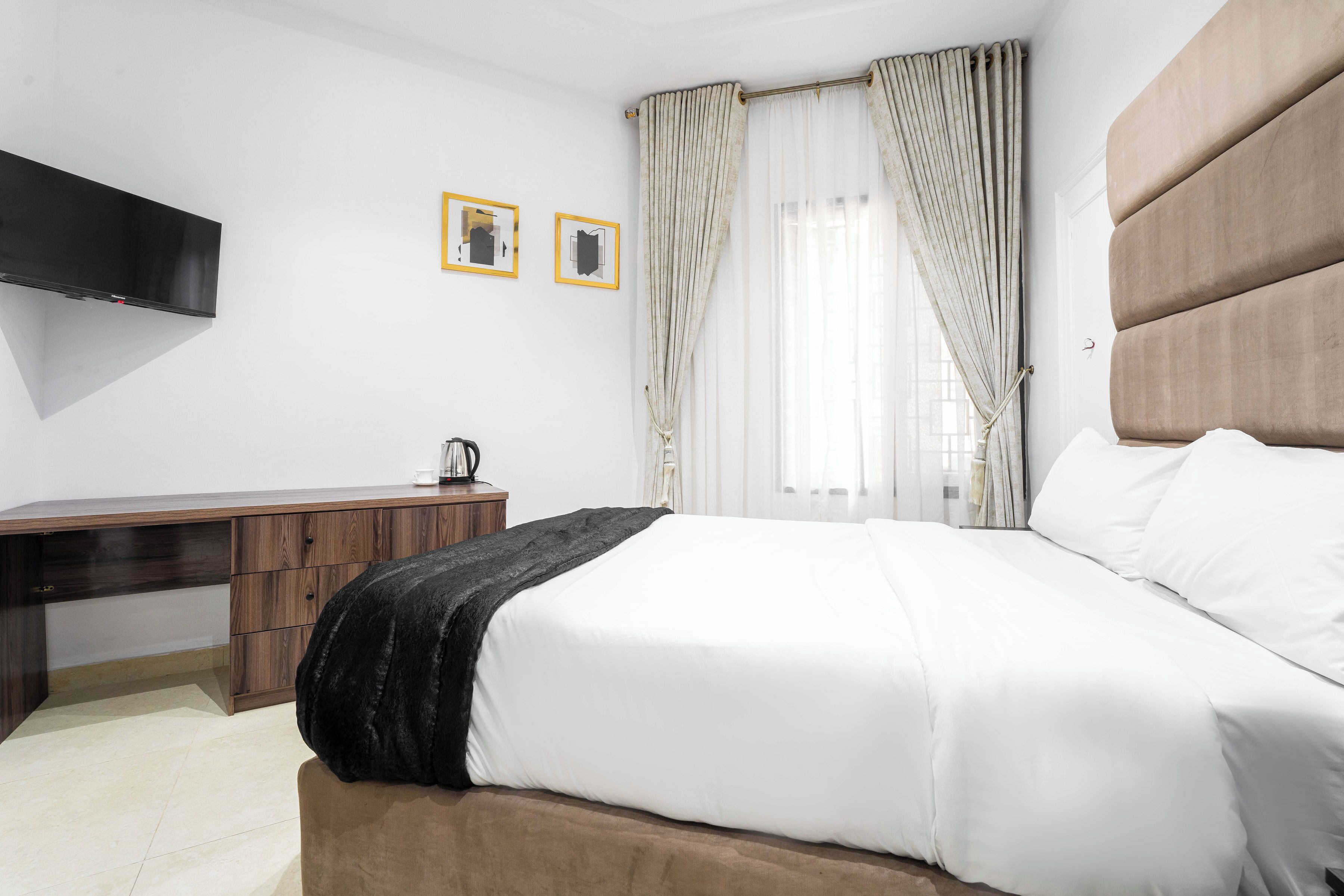 A hotel room with a bed, a desk, a flat-screen TV, and two framed pictures on the wall.