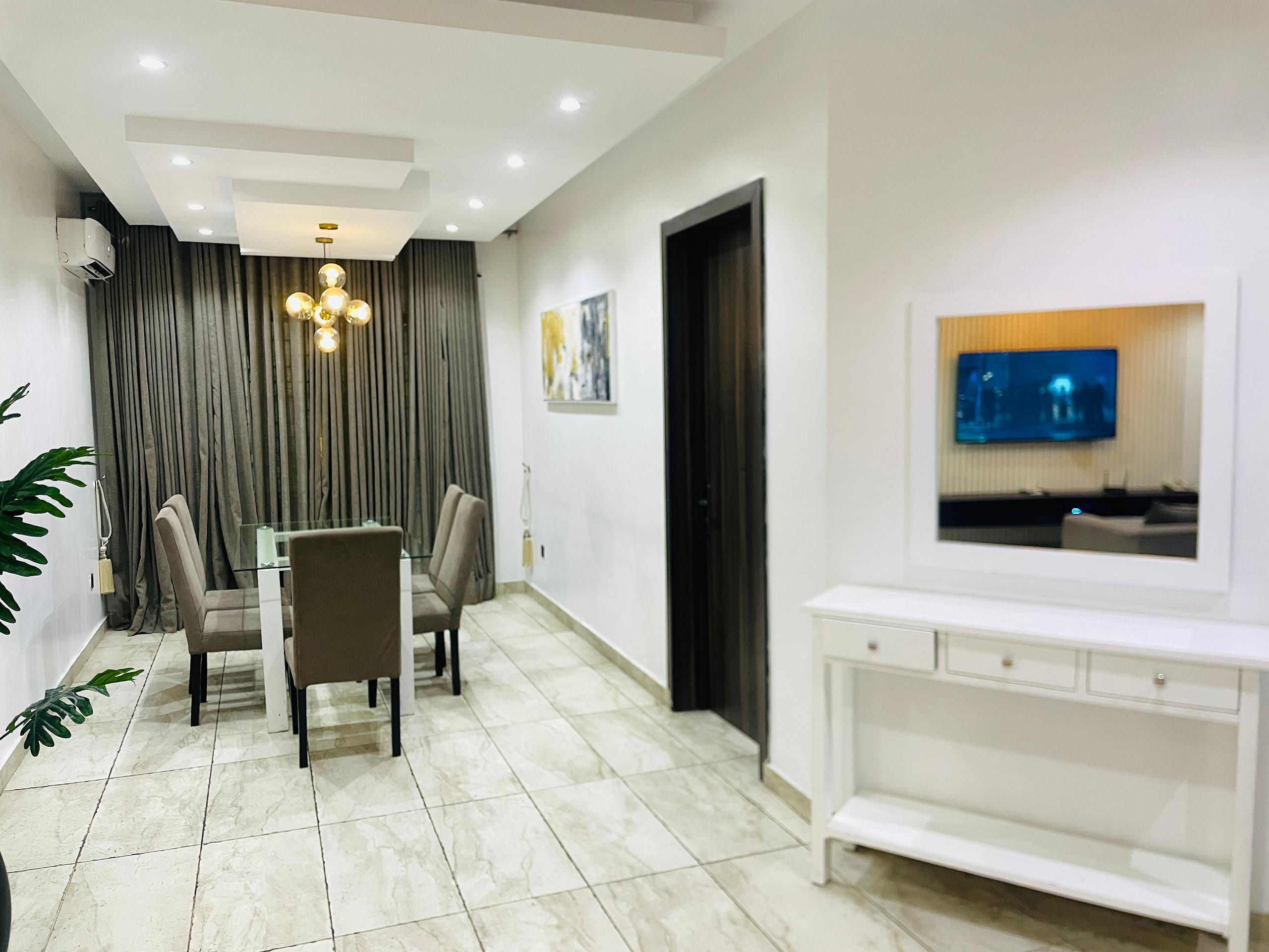 A modern living room with a dining area, a TV mounted on the wall, and a white console table.