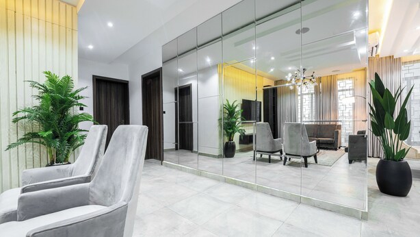 En modern entréhall med en sittgrupp, en stor spegel som reflekterar inredningen och krukväxter.
