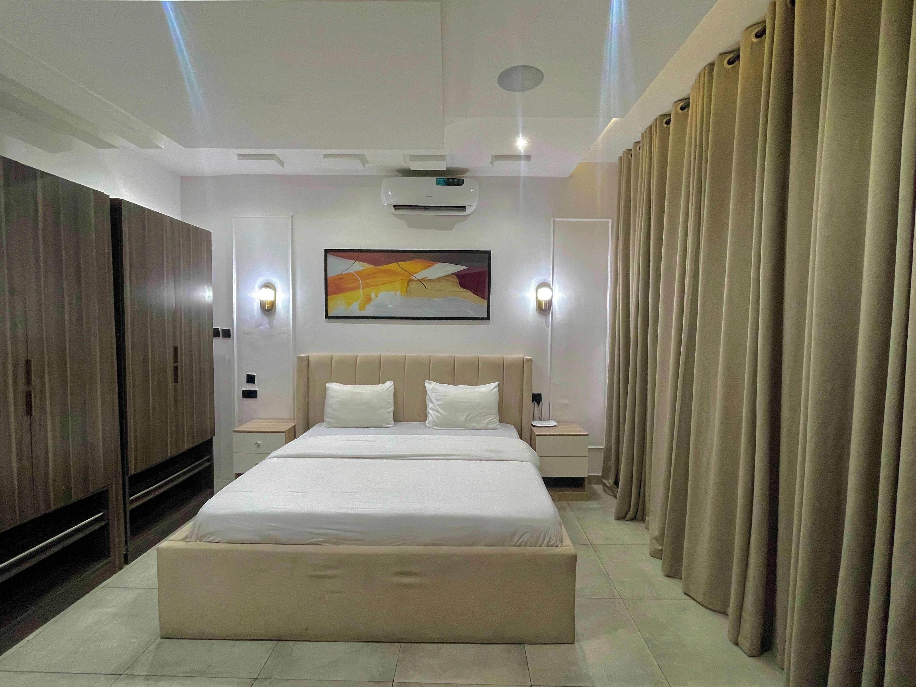 Een moderne hotelkamer met een groot bed, een kledingkast, een nachtkastje en een wandairconditioner.