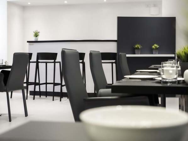 Un espace de restauration moderne avec des chaises noires et une longue table dressée pour un repas.