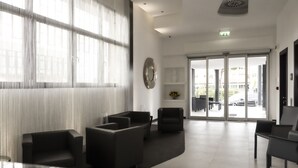 Un área de espera moderna con un ventanal grande, un mostrador de recepción y una zona de estar con sofás y sillones.