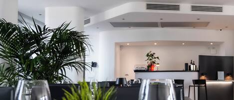 Un comedor moderno con una mesa dispuesta para dos personas, con copas de vino y una planta en maceta.