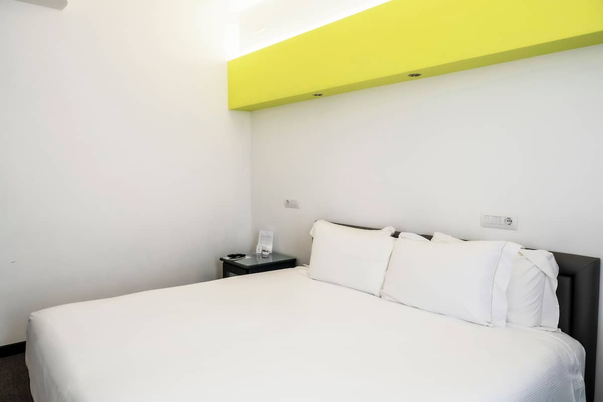 A hotel room with a bed, a nightstand, and a wall socket.