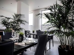 Un espace repas moderne avec des meubles noirs, une table en verre et des plantes en pot.
