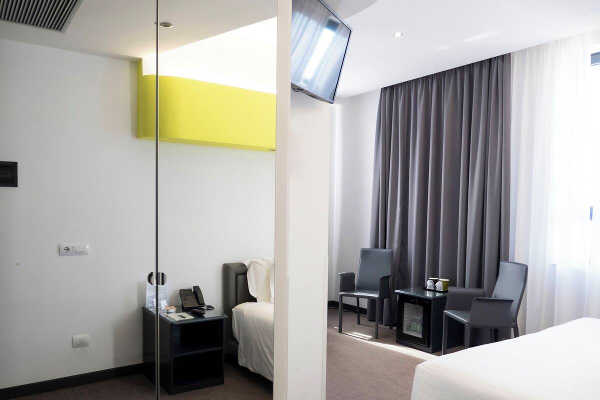 A hotel room with a bed, a desk with a chair, a telephone, and a television mounted on the wall.