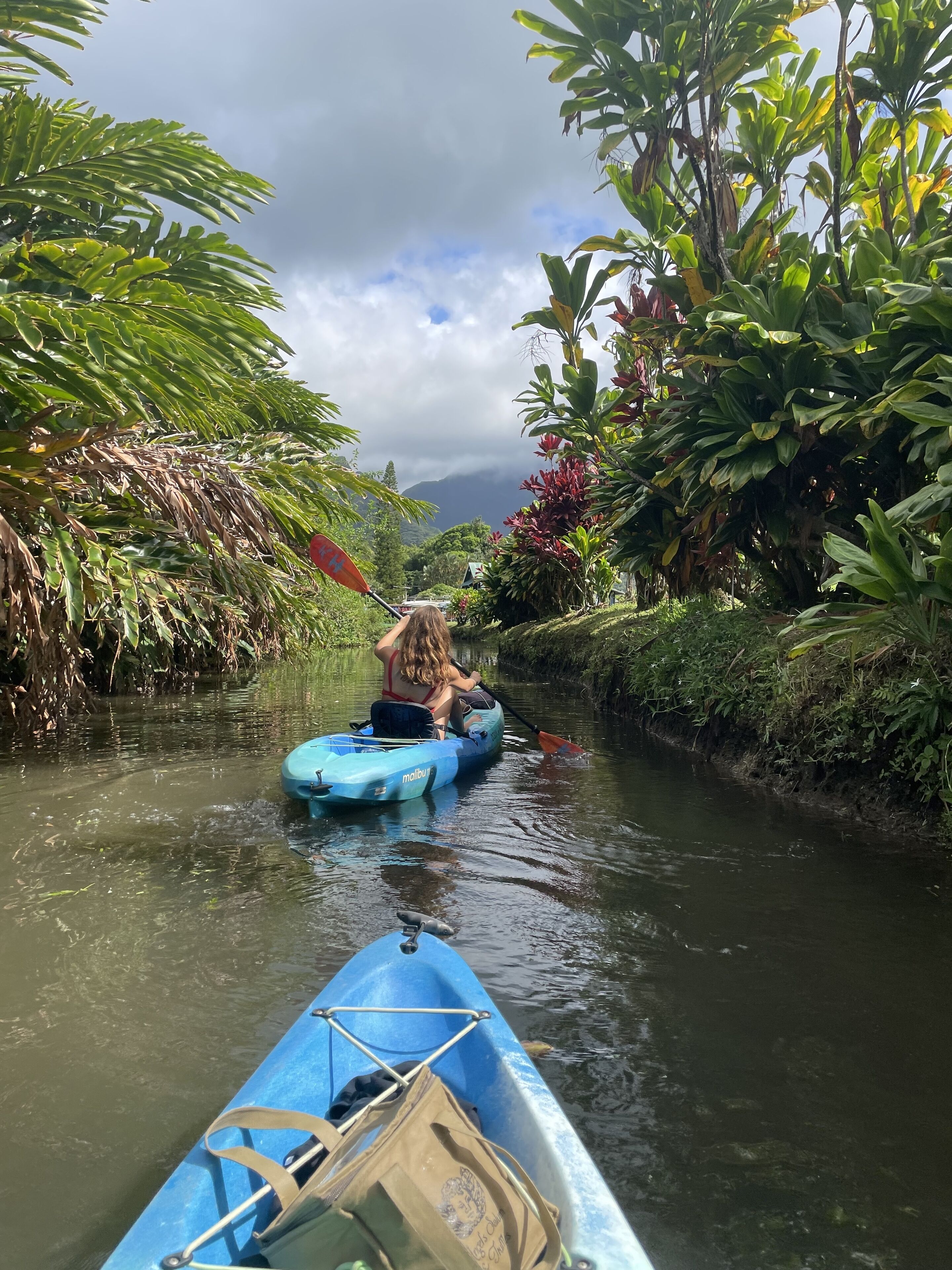 A narrow waterway with a person paddling a blue kayak.