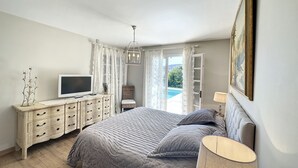 A bedroom with a bed, a TV, a dresser, and a view of a swimming pool. - Spacious villa in town center, large swimming pool, Esterel view (Mandelieu-la-Napoule)