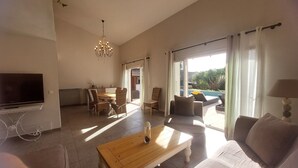 A spacious living room with a television, dining area, and a view of a swimming pool. - Spacious villa in town center, large swimming pool, Esterel view (Mandelieu-la-Napoule)