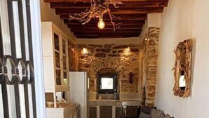A cozy interior with a stone wall, a kitchen with a sink and a television, and a sofa with pillows. - 1875 panoramic stone house (Filoti)