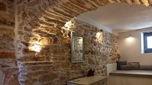 A room with a stone wall, a bed with a headboard, a dresser, and a window with a view. - 1875 panoramic stone house (Filoti)