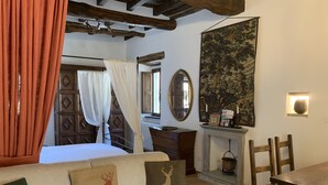 A cozy room with a bed, a wooden table, a sofa with deer-themed cushions, a fireplace, and a large tapestry on the wall. - Vicar's Tower-Maghinardo living in history like a fairy tale.... (Palazzuolo Sul Senio)
