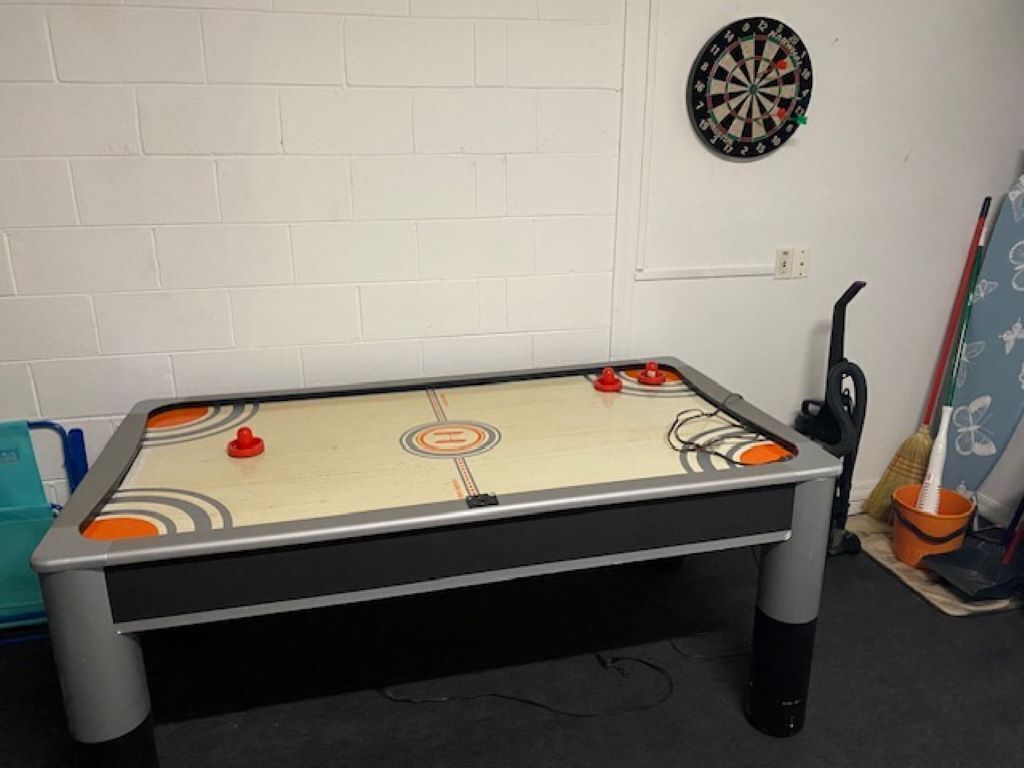 A foosball table with a dartboard and broom in the background.