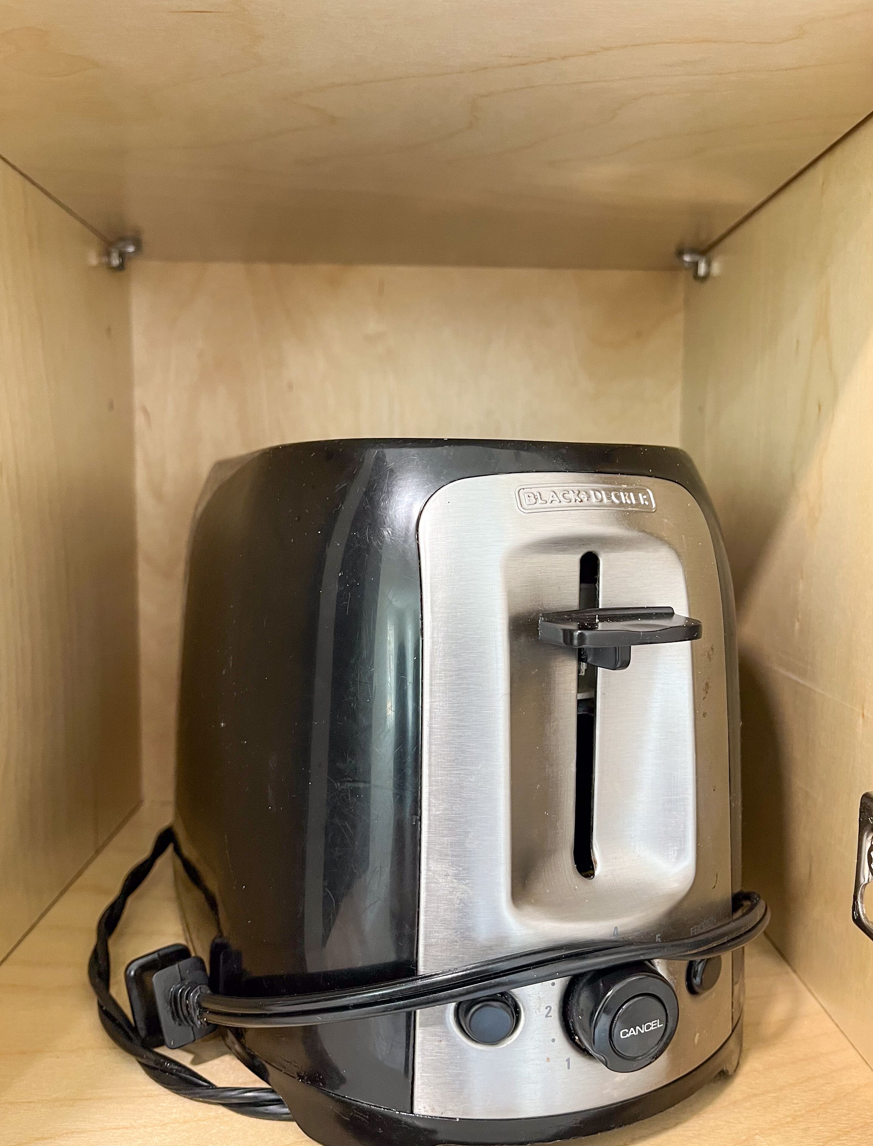 A toaster with a black exterior and a metallic front panel, placed inside a wooden cabinet.