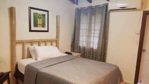 A bedroom with a bed, a nightstand, a framed picture on the wall, and a window with curtains. - Sea View One-Bedroom Apartment in St. Thomas

 (Charlotte Amalie West)