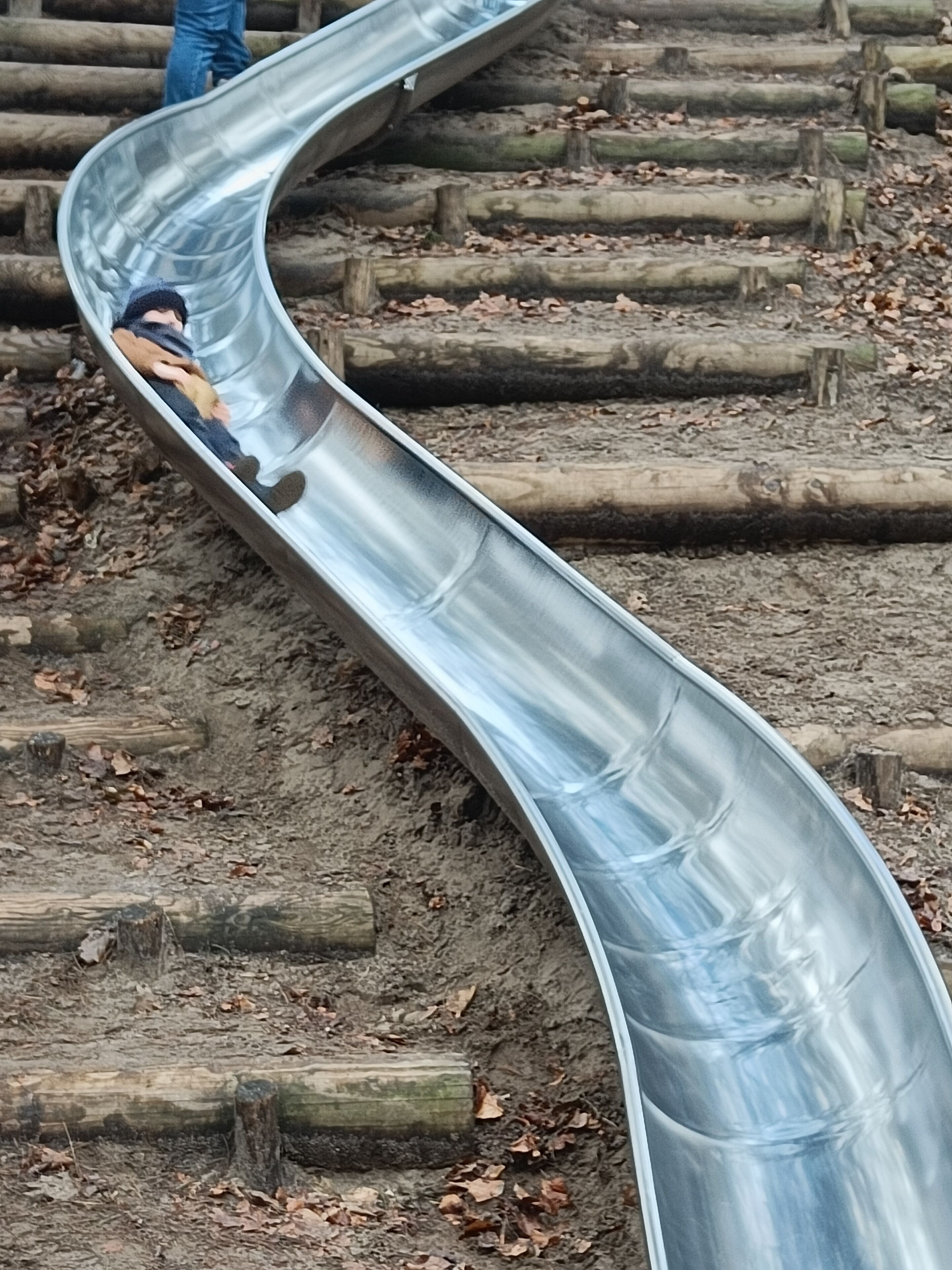 Um escorrega de metal em um parque, com degraus e troncos de madeira.